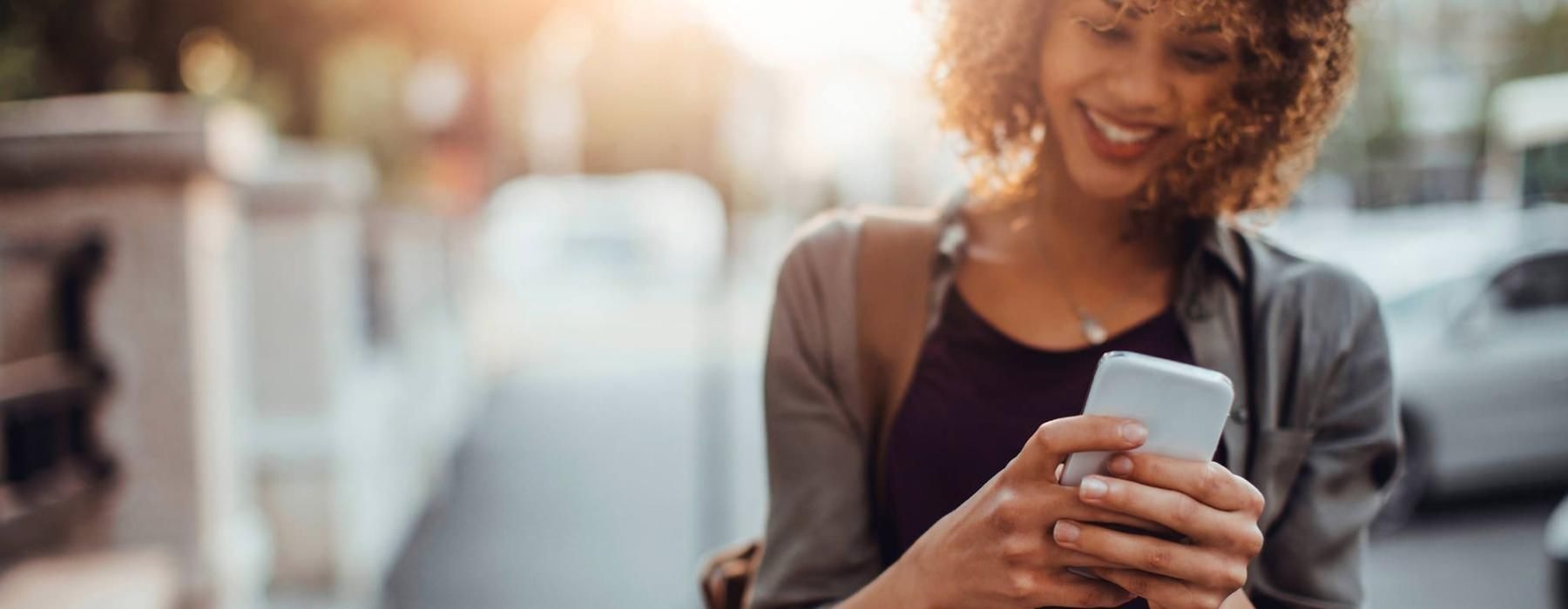 woman texts on her phone as she walks through the city